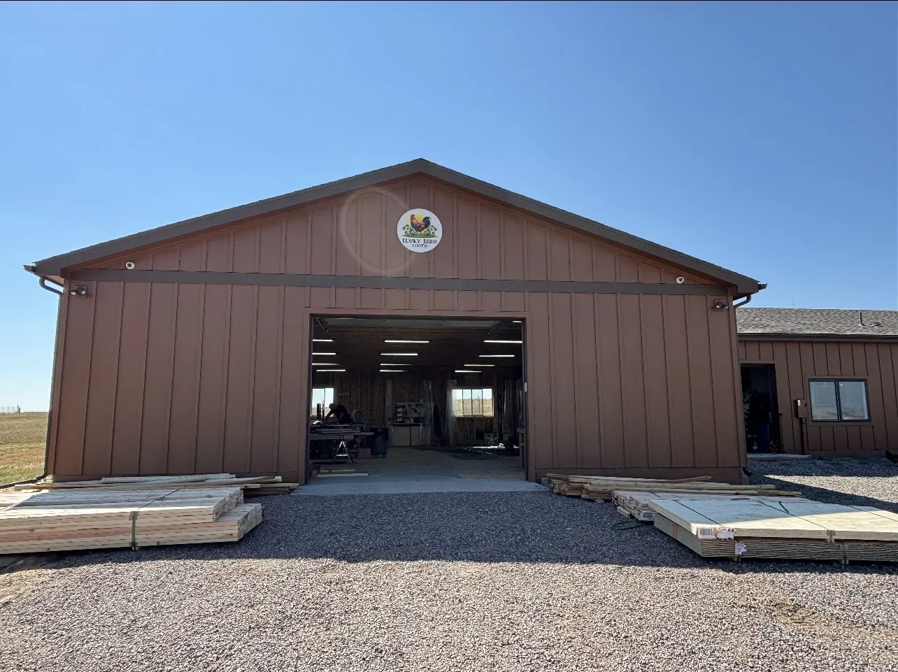 The front of the LuckyBird Coops workshop in Franktown, Colorado — lumber stacked outside the open bay doors